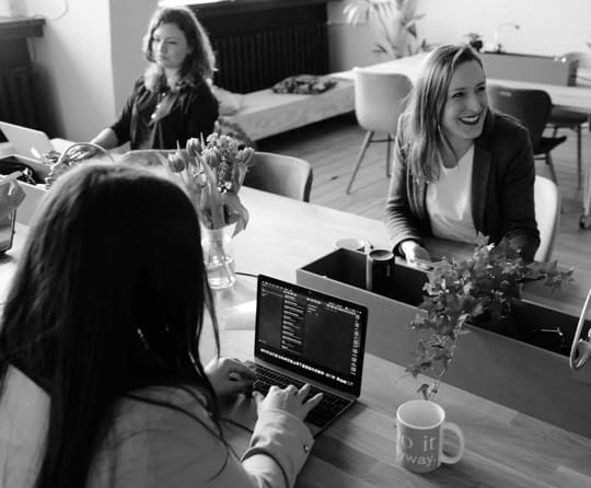 Three women working on laptops at a communal desk