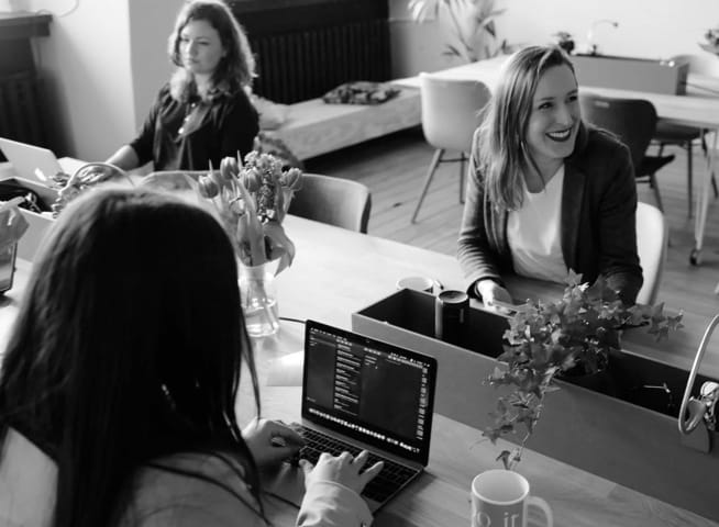 Three women working on laptops at a communal desk